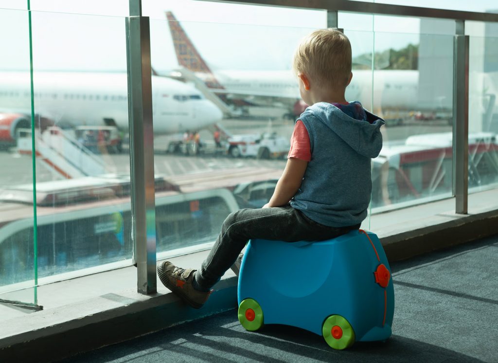 Kind auf seinem Koffer am Flughafen